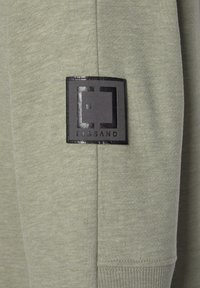 Light green sweatshirt fabric with a textured finish. Features a black embossed logo patch reading "ELBSAND" sewn on the sleeve.