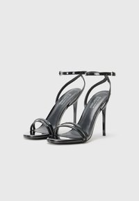 Schwarze Lackleder-High-Heel-Sandaletten mit zwei vorderen Riemen und einem Knöchelriemen, ausgestattet mit einem dünnen Stiletto-Absatz und einer glatten Oberfläche.