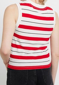 Haut sans manches rayé rouge et blanc avec des lignes noires, doté d'un col rond et d'une coupe ajustée. Matériau en coton doux, style décontracté.