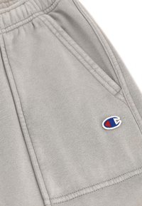 Lichtgrijze sweatshorts met een elastische tailleband, zijzakken en een klein geborduurd logo met rode en blauwe accenten. Zachte textuur.