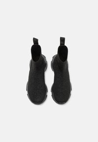 Une paire de baskets slip-on en tricot noir avec des dessus texturés et des semelles en caoutchouc épaisses, vue de dessus sur un fond blanc uni.