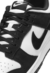 Čierno-biele Nike tenisky s text�úrovaným koženým vrchom, semišovými akcentmi a čiernymi šnúrkami, s perforáciami na špičke.