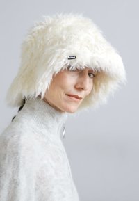Kapelusz bucket z futerkiem syntetycznym w odcieniu kremowym, z szerokim rondem, ozdobiony dyskretną metką marki z boku. Miękka tekstura, unikalny kształt i swobodny design.