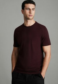 Tricou burgund cu mânecă scurtă și guler rotund, realizat dintr-un material neted, conceput pentru a avea o siluetă ajustată.