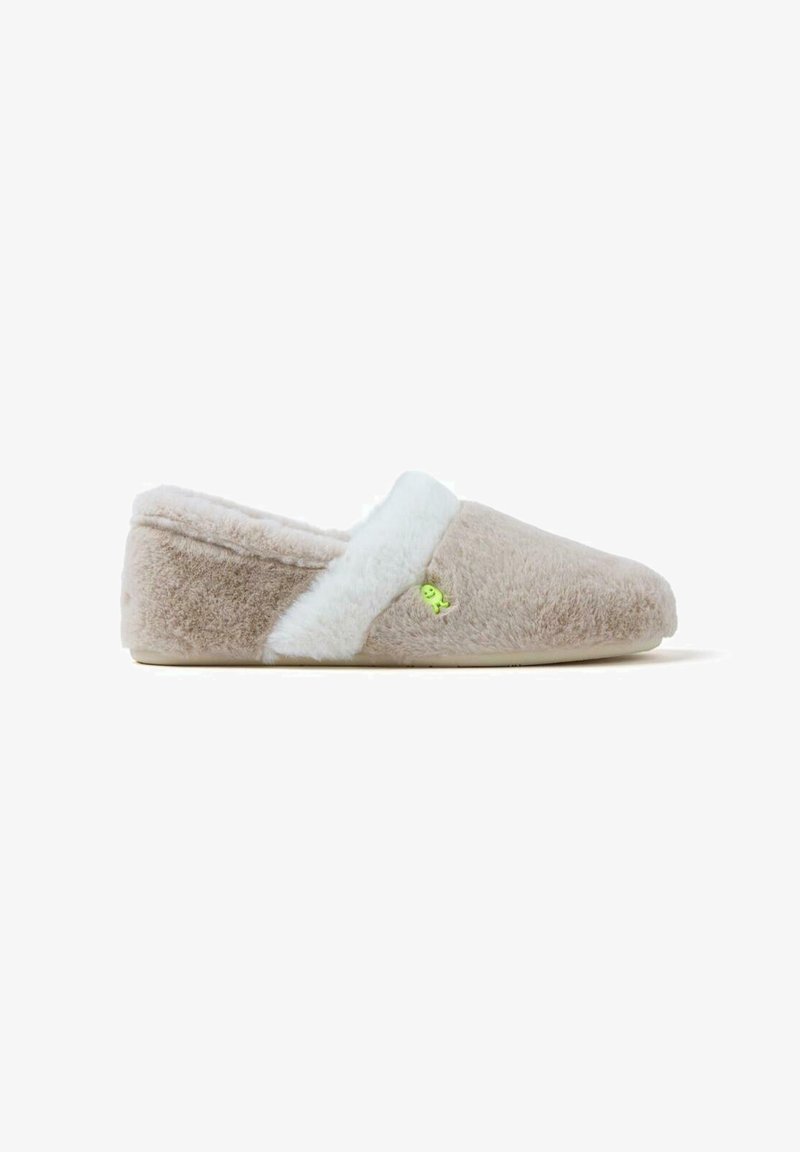 Chausson beige en matériau doux et pelucheux avec une bordure en fausse fourrure blanche, présentant un petit détail de design vert sur le côté.