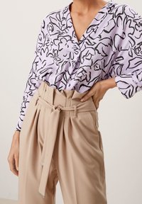 Långärmad blus i ljus lavendel med svart blommönster, i kombination med högmidjade beige byxor med knytbälte och veckad front.