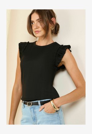 Fekete, bordázott felső fodros ujjakkal, kerek nyakkivágással. Világoskék, magas derekú farmernadrággal és fekete övvel párosítva. Arany karkötő kiegészítő.