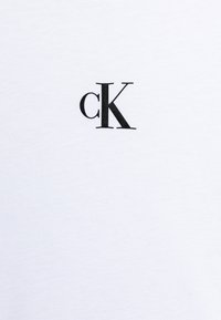 Biała bawełniana koszulka z czarnym logo "cK" nadrukowanym na lewej piersi. Gładka tekstura, okrągły dekolt i krótkie rękawy.