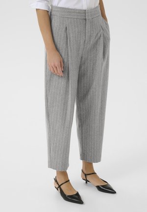 Model wears grey pinstriped trousers with a relaxed fit, paired with black slingback heels, standing against a plain white background.