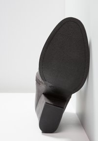 Bota negra hasta el tobillo con una parte superior de tejido texturizado, un tacón moderado y una suela de goma, con cremallera lateral para facilitar su uso.