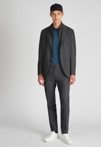 Grau maßgeschneiderter Anzug mit strukturiertem Stoff, kombiniert mit einem einfarbigen blauen Hemd und weißen Schuhen. Zubehör umfasst eine schwarze Mütze. Minimalistisches Design.