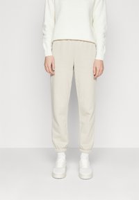Beige joggebukser med elastiske mansjetter, mykt bomullsstoff, parret med en teksturert hvit genser og hvite sneakers.