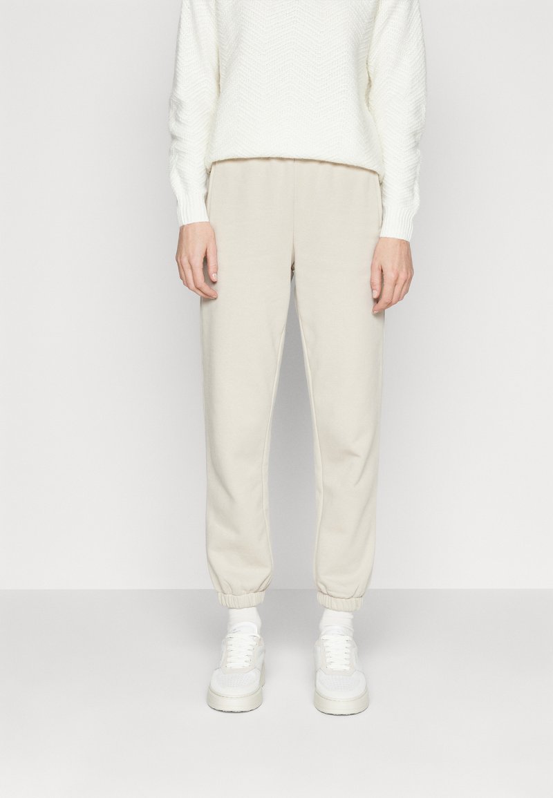 Beige joggebukser med elastiske mansjetter, mykt bomullsstoff, parret med en teksturert hvit genser og hvite sneakers.