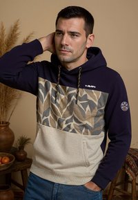 Hoodie met donkerblauwe mouwen en een beige middenstuk, met een bladerenpatroon. Inclusief een voorzak en een trekkoord.