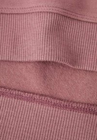 Tessuto rosa con una texture morbida, caratterizzato da un bordo a costine e uno strato interno liscio. Le cuciture sono visibili lungo i bordi.
