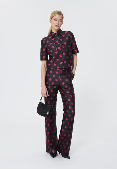 Must have musta riidekomplekt, millel on roosa südame muster; lühikeste varrukatega lühike särk ja laiad püksid. Modell hoiab käes väikest musta sädeleva käekotti.