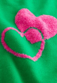 Green fabric with raised pink heart shapes and outlines. Soft, fuzzy texture with contrasting smooth areas.