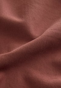 Terracotta stof med en blød, glat tekstur, der har et let udseende og en subtil, jævn struktur. Ingen synlige mønstre eller accenter.