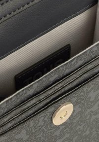 Interior de un monedero de cuero texturizado gris con forro de tela suave, que cuenta con un cierre a presión y una etiqueta de marca visible.