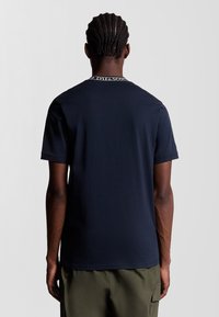 Mørkeblå bomulds t-shirt med korte ærmer, med en rund halsudskæring og et kontrastfarvet logo bånd omkring kraven. Glat tekstur.