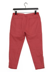 Pantaloni in tessuto stretch rosso con una texture liscia, dotati di aperture con zip a livello caviglia e due tasche posteriori, appesi a una gruccia nera.