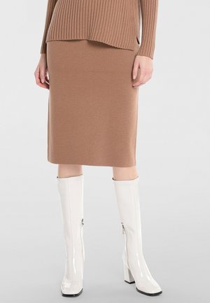 Jupe midi en tricot marron avec une finition texturée, associée à des bottes blanches brillantes jusqu'au genou avec une fermeture éclair sur le côté et des talons hauts à bloc.