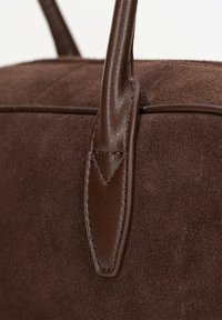 Bruine suède tas met leren handvatten. Beschikt over een gladde textuur, subtiele stiksels en een gestructureerde vorm.