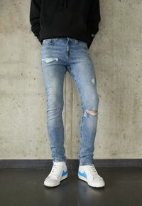 Bleknade blå skinny jeans med rivna detaljer. Bärs med vita sneakers med blå accent, i kombination med en svart hoodie.