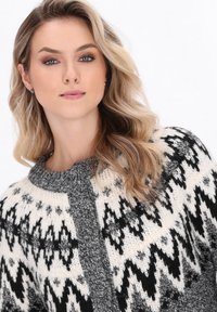 Zwart-wit gestreepte gebreide cardigan met een contrasterende grijze knopenlijst en een ronde halslijn. Zachte textuur, losse pasvorm en gedetailleerd ontwerp.