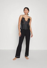Camisole en satin noir avec bordure en dentelle, associée à un pantalon noir à piping blanc aux ourlets. Les deux articles ont une coupe décontractée.