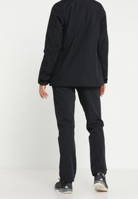 Black outdoor jacket and pants made of textured, water-resistant material. Jacket features a straight cut; pants have a slim fit.