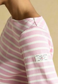 Wzorzysta bluzka z długim rękawem w jasnoróżowym i białym kolorze. Posiada okrągły dekolt oraz metkę z danymi marki na lewym ramieniu.