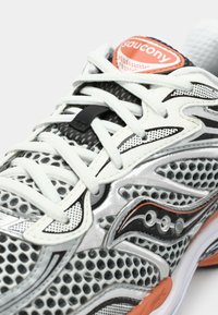 Silver athletic shoe with mesh upper, black accents, and orange logo. Features a padded tongue and textured sole for grip.