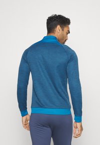 Blaues, athletisches Langarmshirt aus strukturiertem Stoff, mit hohem Kragen und kontrastierenden blauen Bündchen. Gerippter Saum und Akzente an den Ärmeln.