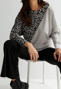 Šedý a černý dlouhý rukáv s leopardím potiskem na jedné straně, doplněný černými kalhotami a kotníkovými botami. Texturovaná tkanina.