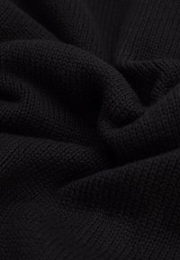 Czarna dzianina, ukazująca teksturowany wzór z miękkim, gładkim wykończeniem, fałdy i zmarszczenia tworzące głębię i wymiar.