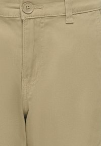 Beige Baumwollhose mit glatter Textur, mit einem Knopfverschluss und dezenten Nähten. Vordertasche auf der linken Seite sichtbar.