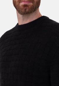 Schwarzer Strickpullover mit strukturiertem Muster und geripptem Rundhalsausschnitt. Warmes Material und dicht gewebtes Detail sind sichtbar.