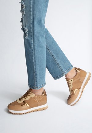 Sneakers marroni chiari con accenti in oro metallico, pannelli in rete e lucidi, abbinati a jeans blu strappati, che mostrano uno stile casual.