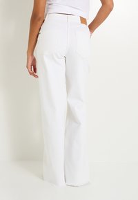 Jeans anchos blancos con cintura alta, dobladillo deshilachado y dos bolsillos traseros. La tela es un denim resistente con detalles de diseño minimalistas.