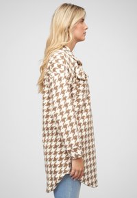 Jachetă din flanel cu model houndstooth în nuanțe de maro și crem, cu un croi lejer, închidere cu nasturi și fante laterale pentru un plus de confort în mișcare.