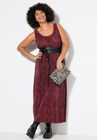 Maxikleid in Rot mit schwarzem Tiermotiv, ausgestattet mit einem schwarzen Taillengürtel, kombiniert mit einer Clutch im Zebra-Muster und schwarzen klobigen Stiefeln.