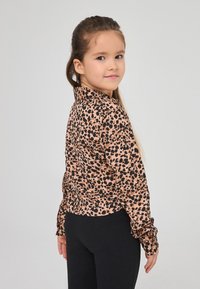 Maglia a maniche lunghe con una base rosa e motivo leopardato nero, dotata di colletto e manicotti arricciati, abbinata a leggings neri.