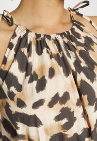 Haalari yläosa, jossa on leopardi-kuvio, valmistettu pehmeästä ja kevyestä kankaasta. Ominaisuuksiin kuuluu rypistynyt kaula-aukko ja säädettävät siteet olkapäillä vaaleanruskeana ja tummanruskeana.