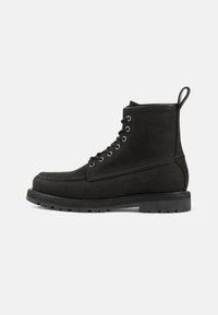 Botas de cuero negras hasta el tobillo con punta redonda, diseño de cordones, ojales de metal y suela de goma texturizada. Cuenta con una lengüeta decorativa.