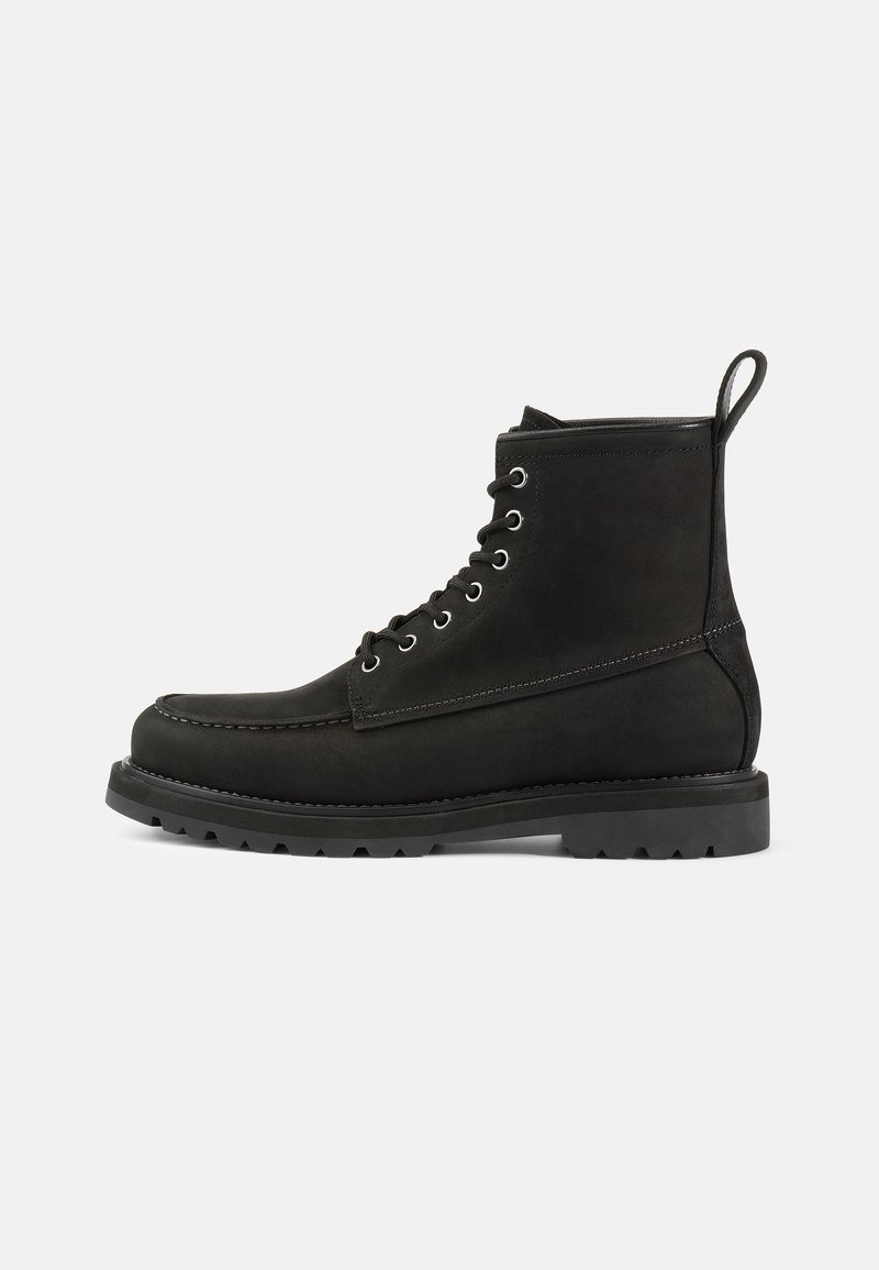 Botas de cuero negras hasta el tobillo con punta redonda, diseño de cordones, ojales de metal y suela de goma texturizada. Cuenta con una lengüeta decorativa.