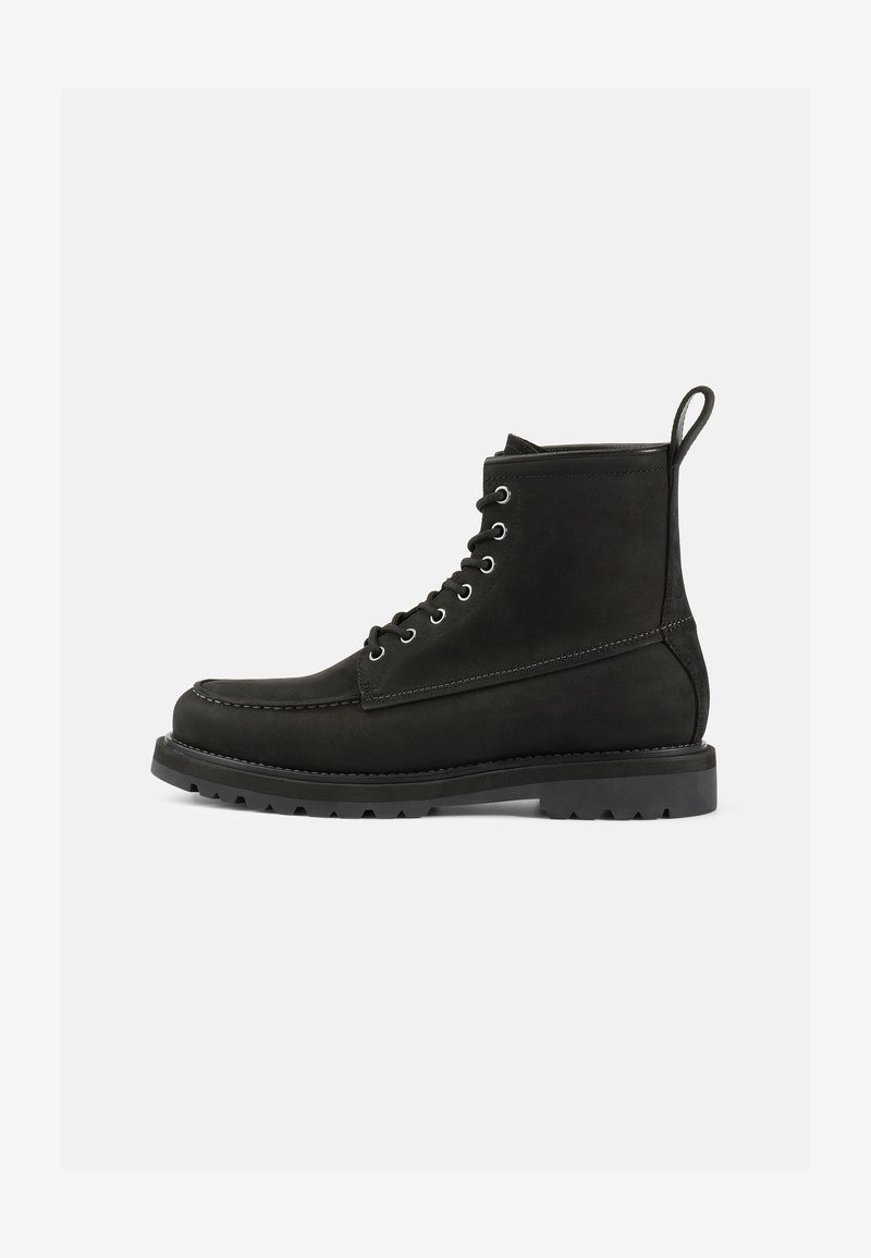Botas de cuero negras hasta el tobillo con punta redonda, diseño de cordones, ojales de metal y suela de goma texturizada. Cuenta con una lengüeta decorativa.