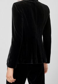 Musta samettinen bleiseri, jossa pitkät hihat, vartalonmyötäinen malli ja hillitty kiilto. Mallissa on lantiolla liehuke ja sileä, pehmeä pinta.