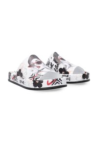 Grafische slippertjes met een witte basis en een zwart-rode bloemenpatroon, en een gestileerde gezichtillustratie. Open neus en platte zool.