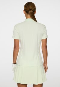 Mintgrünes kurzärmeliges Poloshirt mit Kragen, das über ein strukturiertes Muster und ein gefaltetes, ausgestellt gestaltetes unteren Ende verfügt.